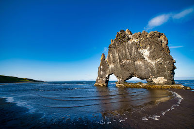 Scenic view of rock formation in sea against blue sky