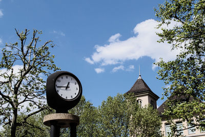 Low angle view of clock by trees against sky