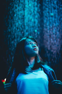 Woman looking away against illuminated waterfall at night