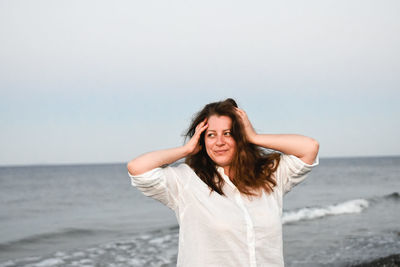 Portrait of young woman standing at beach against clear sky