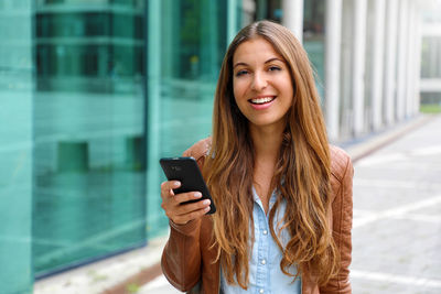 Smiling woman using smart phone while standing in city