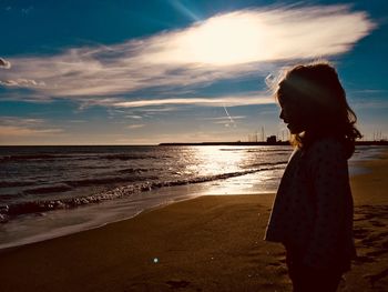 Woman standing at beach against sky during sunset