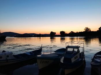 Boats moored in lake against clear sky during sunset