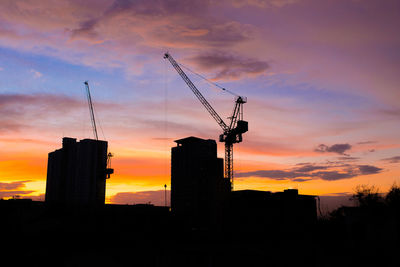 Silhouette crane by building against dramatic sky during sunset