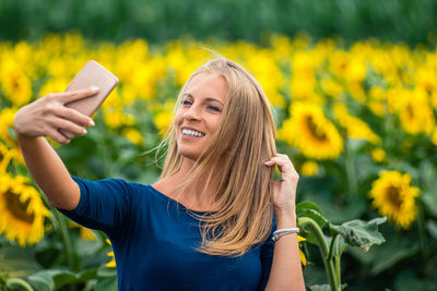 Happy young woman taking selfie through smart phone at sunflower field