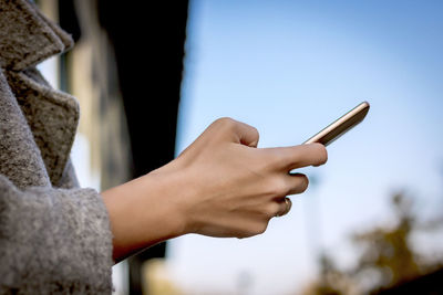 Close-up of woman text messaging on mobile phone outdoors.