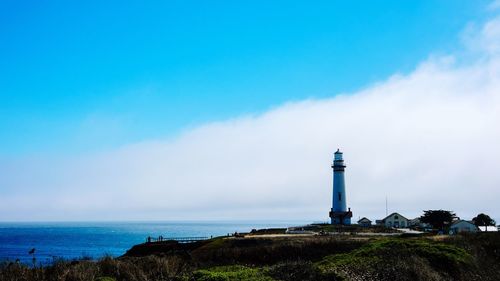 Lighthouse in sea against cloudy sky