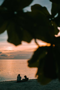 People sitting on beach against sky during sunset