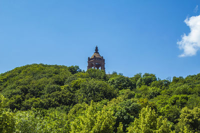 Low angle view of trees and building against blue sky