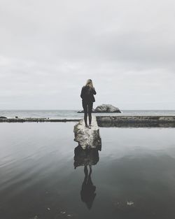 Rear view of woman standing on beach against sky