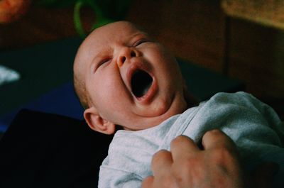 Cropped hand of parent holding baby yawning at home