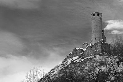 Low angle view of abandoned building on hill against cloudy sky during winter