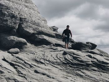Low angle view of man walking on rock formation against cloudy sky