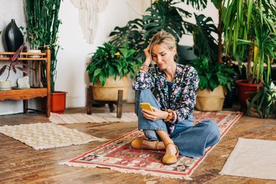 Young relaxed blonde woman sitting on the floor uses phone for online communication.