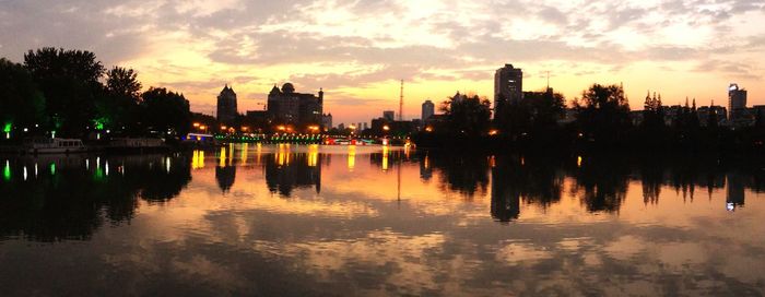 Reflection of silhouette trees and buildings in lake during sunset