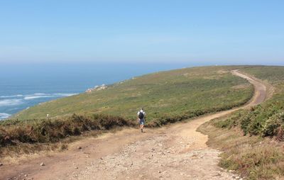 Man walking on dirt road by sea against clear sky