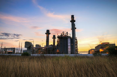 Factory on field against sky during sunset