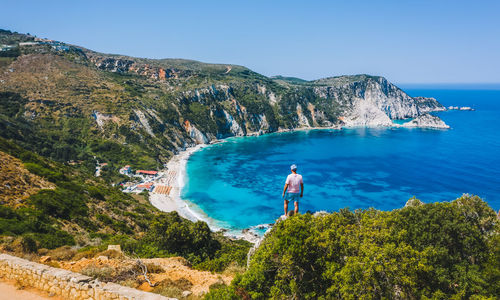 Man looking at sea by mountain against sky