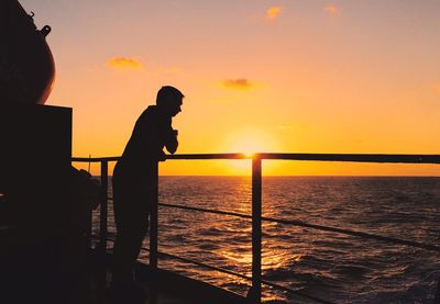 Silhouette man standing by railing against sea during sunset