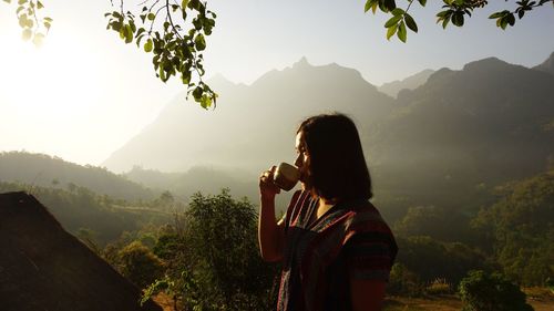 Woman drinking coffee by mountains against sky