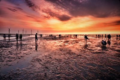 Silhouette people on beach against sky during sunset