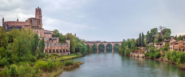 Arch bridge over river amidst buildings against sky