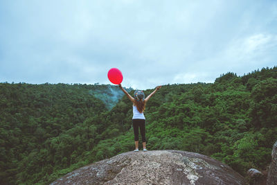 Rear view of woman standing with balloon against trees in forest