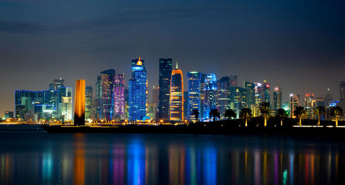 Illuminated modern buildings in city against sky at night