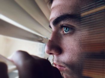 Close-up of young man peeping through blinds