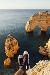 Low section of man wearing shoes resting on cliff against sea