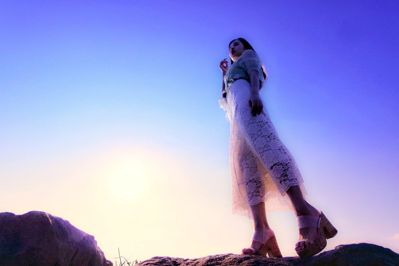 LOW ANGLE VIEW OF WOMAN STANDING ON ROCK AGAINST SKY