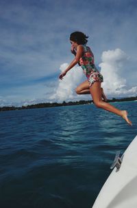 Side view of girl diving into sea against sky