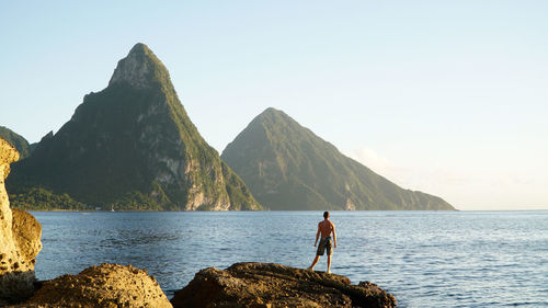 Man standing on rock by sea against clear sky