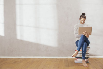 Young woman sitting on stack of books using laptop at home