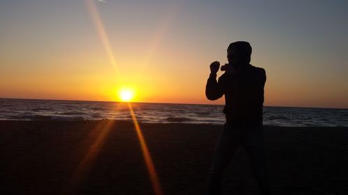 Silhouette woman photographing sea against sunset sky