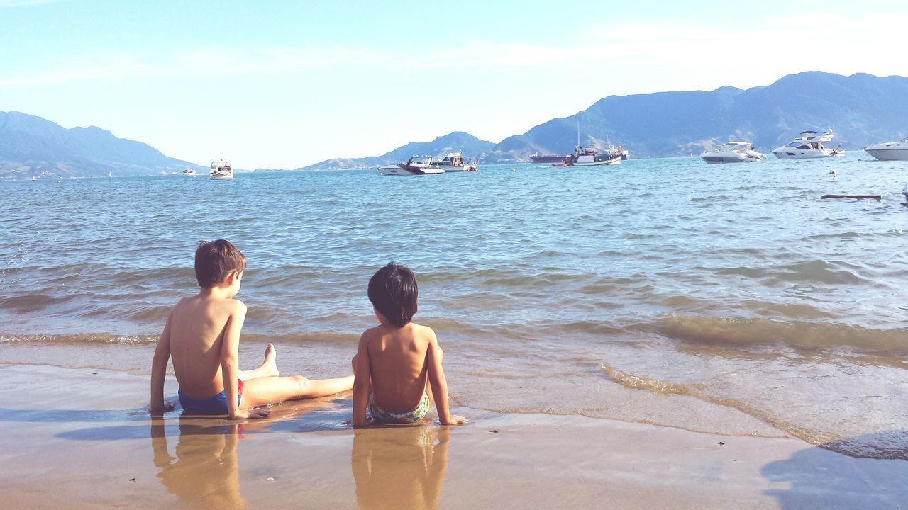 REAR VIEW OF PEOPLE AT BEACH AGAINST SKY