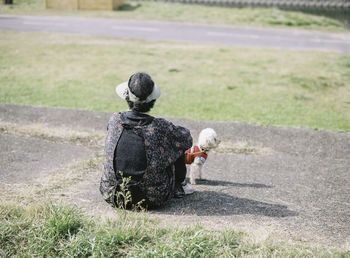 Rear view of person sitting on footpath with dog