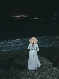 Rear view of woman standing at beach during night