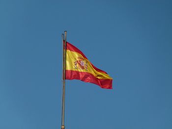 Low angle view of spanish flag against clear blue sky