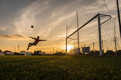 Full length of man playing soccer against sky during sunset