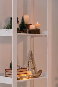 Christmas candles are lit on the shelves next to decorative christmas trees and books.