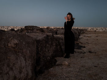 Side view of woman standing on rock against sky