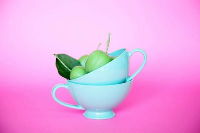 Close-up of apples in cup on pink background