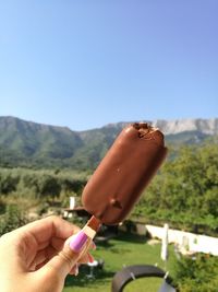 Close-up of woman hand holding chocolate popsicle against clear blue sky