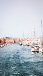 Sailboats in sea by buildings against clear sky