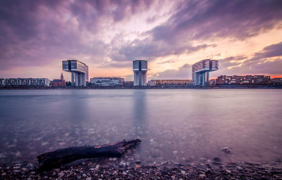 Scenic view of river by buildings against sky at sunset