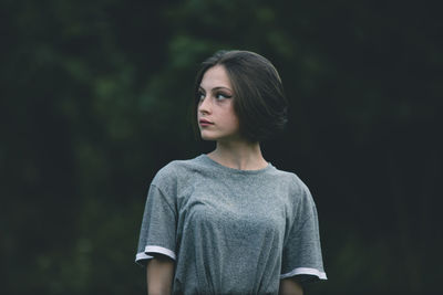 Beautiful young woman looking away against trees