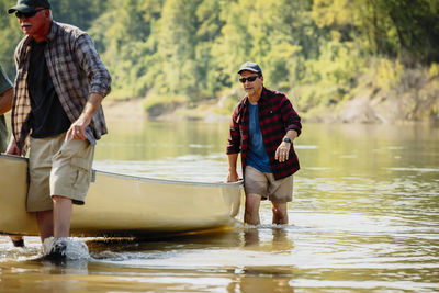 Male friends pushing boat in lake