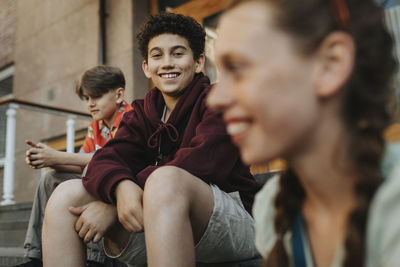 Portrait of smiling boy sitting with friends on staircase of school building entrance