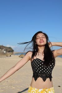 Portrait of young woman standing at beach against clear blue sky